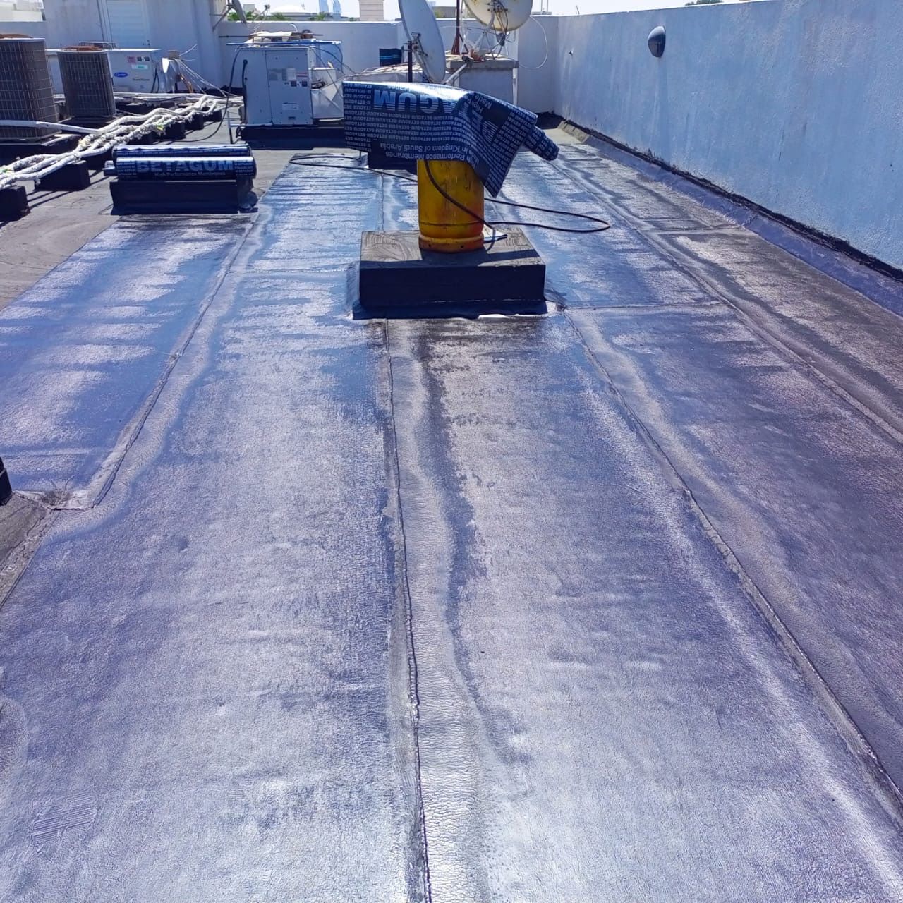 Liquid applied bitumen waterproofing being coated across a Dubai roof